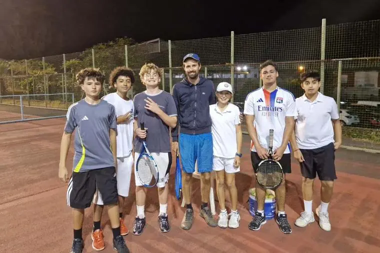 Un coach de l'école de tennis entouré de six jeunes joueurs à la fin d'une séance.